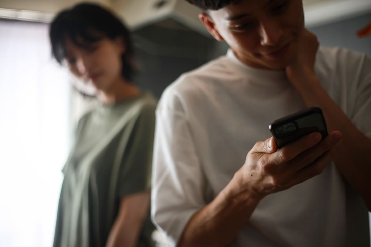 夫がスマホを操作する様子に違和感を覚える妻のイメージ